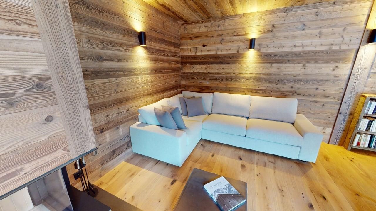 Un salon chaleureux avec des murs en bois clair, un canapé d'angle blanc et une petite table basse en bois.