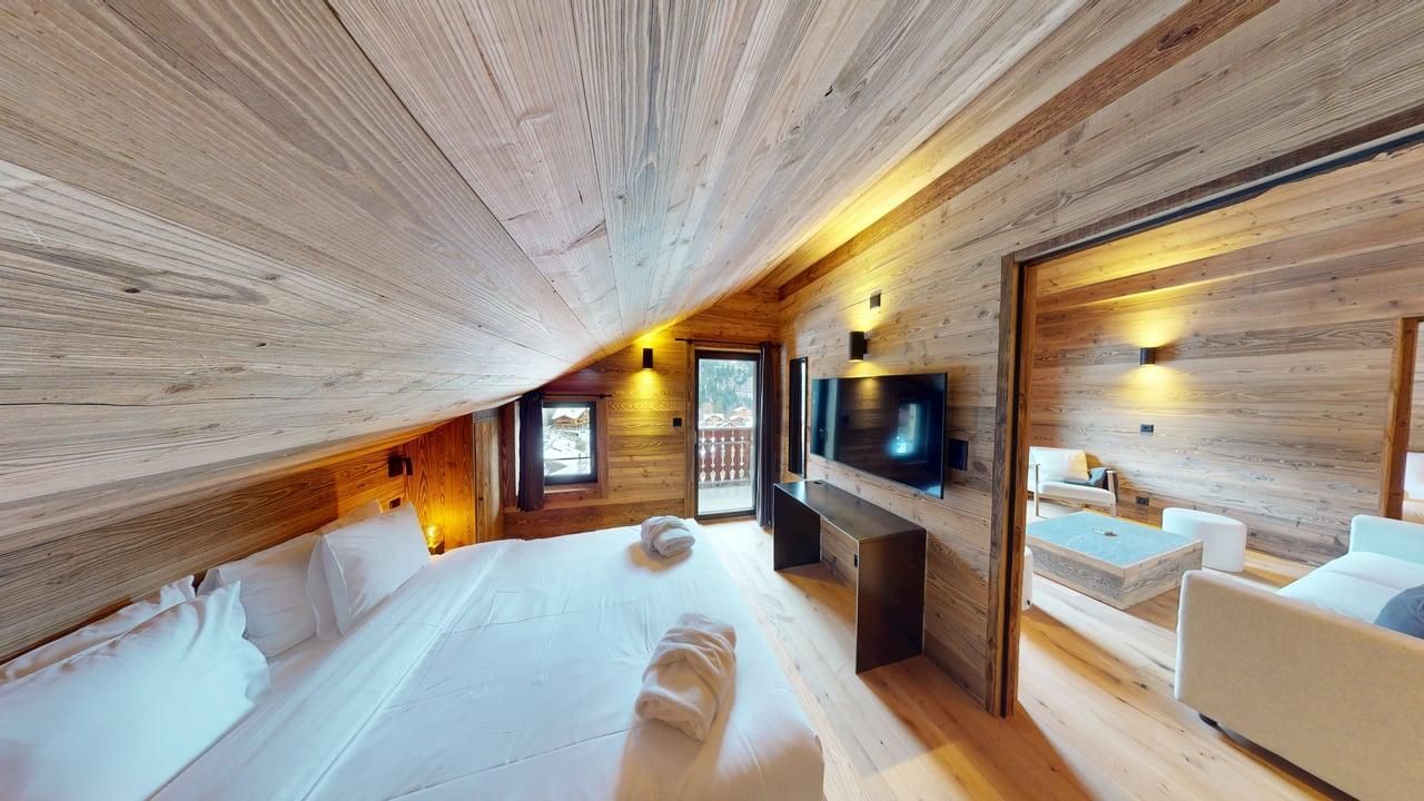 A wood-paneled bedroom with a large bed, TV, and an adjoining living area under a sloped ceiling.