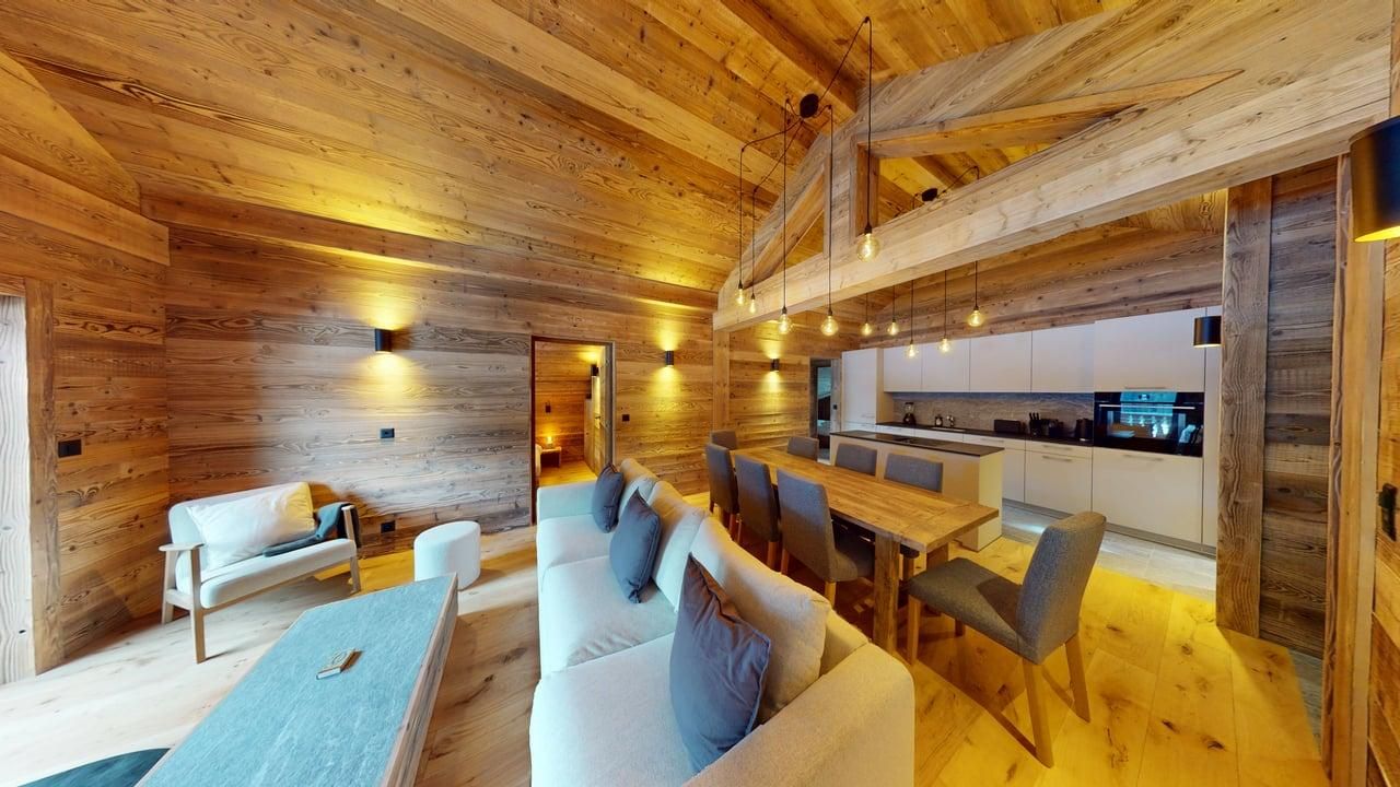 A modern, wood-paneled chalet interior featuring a living area, dining table, and kitchen with warm ambient lighting.