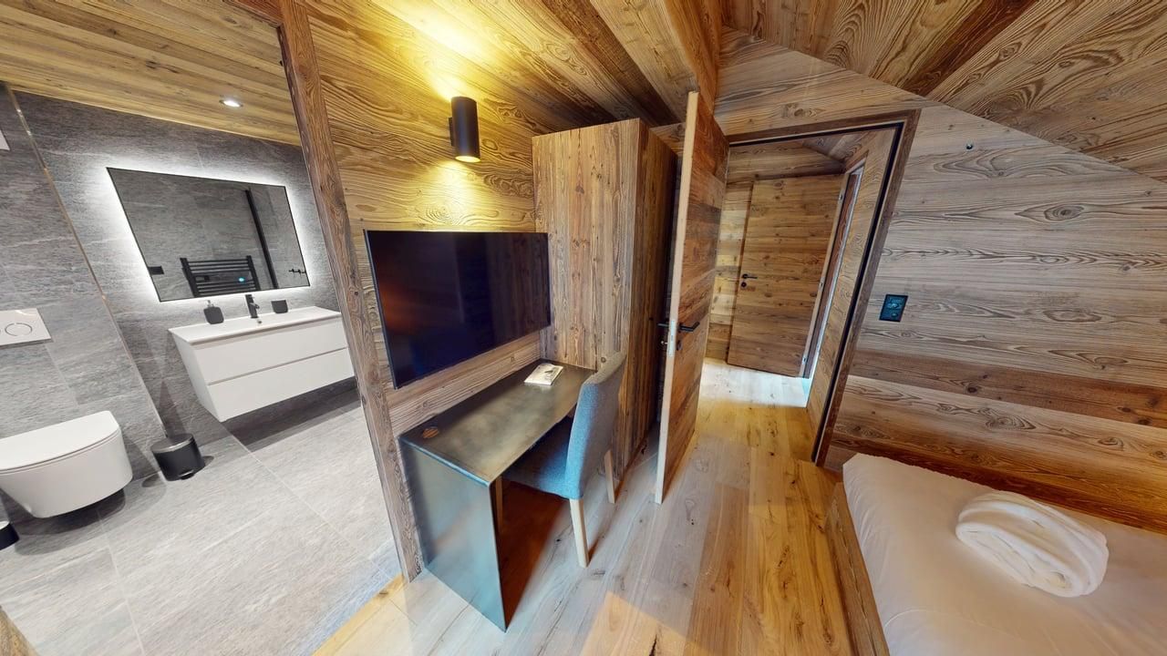 A hotel room featuring a wood-paneled bedroom, a built-in desk, a flat-screen TV, and an adjacent modern white bathroom.