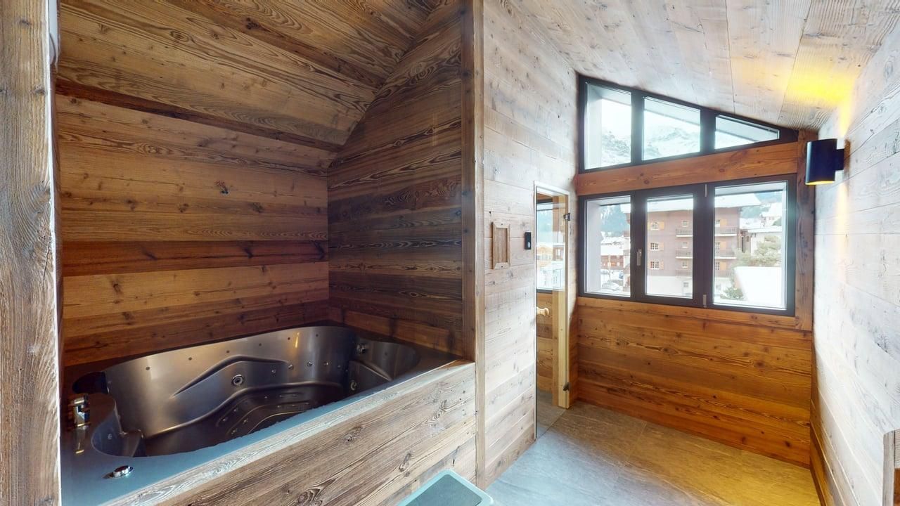 A modern wooden room with a stainless steel jetted bathtub, large windows, and slanted ceilings, resembling a spa area.