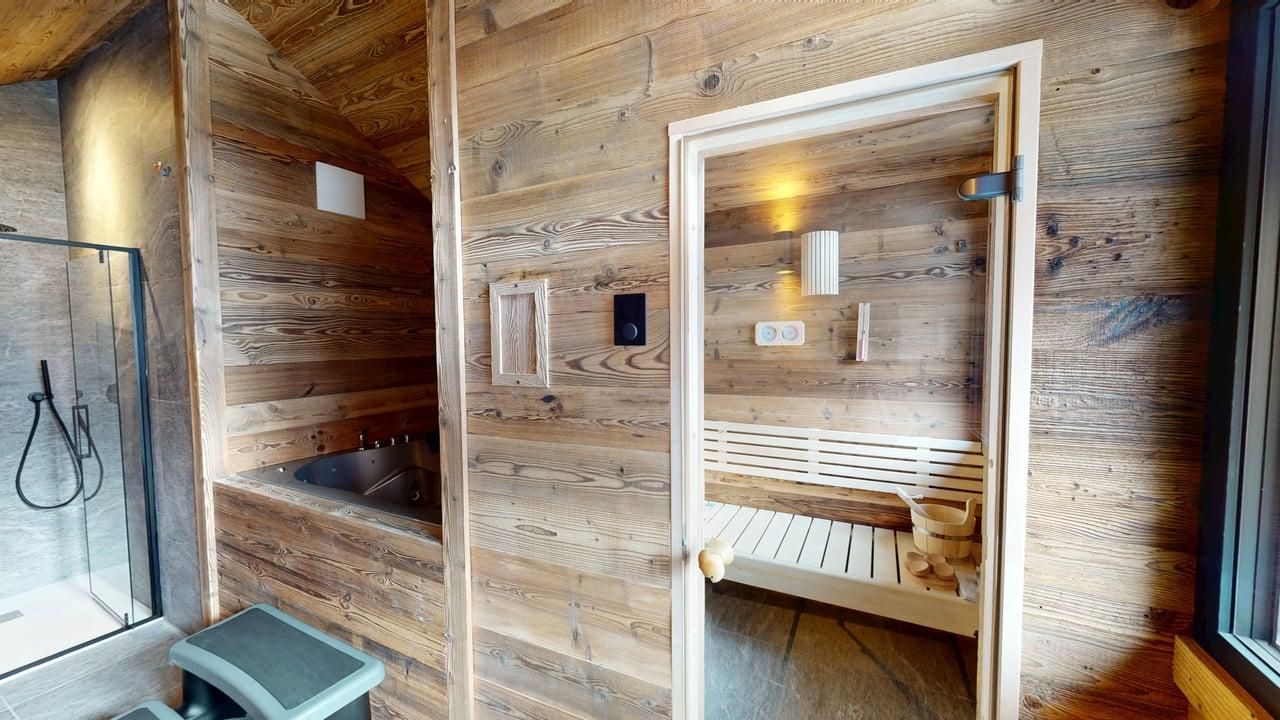 A wood-paneled spa room featuring a shower enclosure, a sauna with a glass door, and a rustic aesthetic.