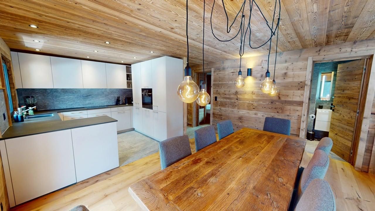 Cuisine et salle à manger modernes avec murs en bois, grande table en bois et placards de cuisine blancs.