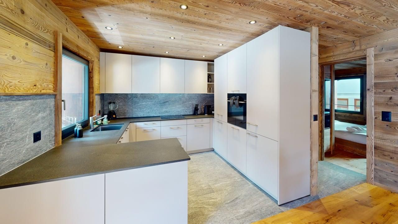 Une cuisine moderne avec des armoires blanches, des comptoirs en pierre foncée et des murs et un plafond lambrissés dans un intérieur rustique.