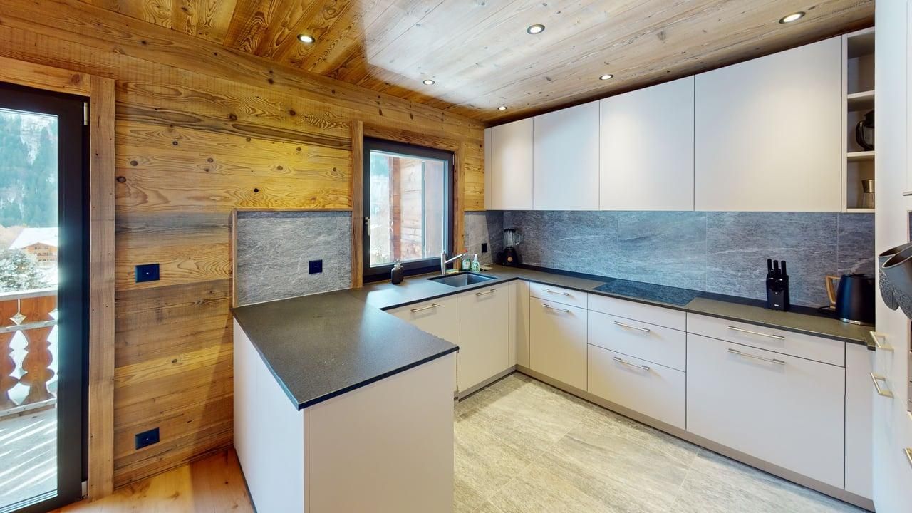 Modern U-shaped kitchen with white cabinets, dark gray countertops, and wood-paneled walls in a mountain-style cabin.