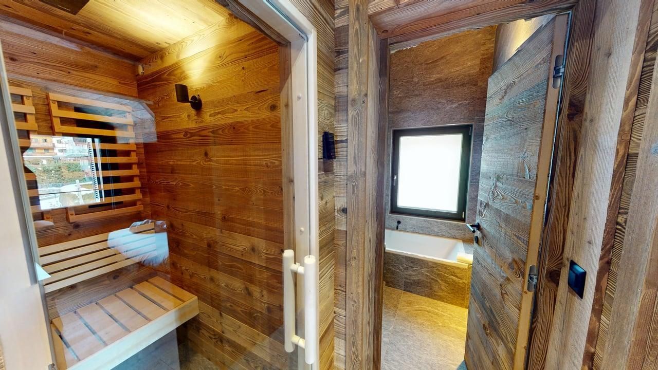 A wood-paneled sauna on the left, open to a bathroom on the right with a bathtub by a window.