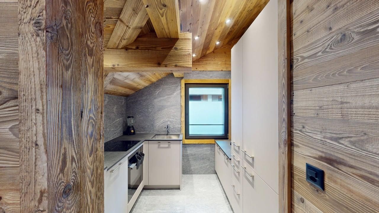 A modern galley kitchen with light cabinets and wood-paneled walls under rustic exposed wooden ceiling beams.