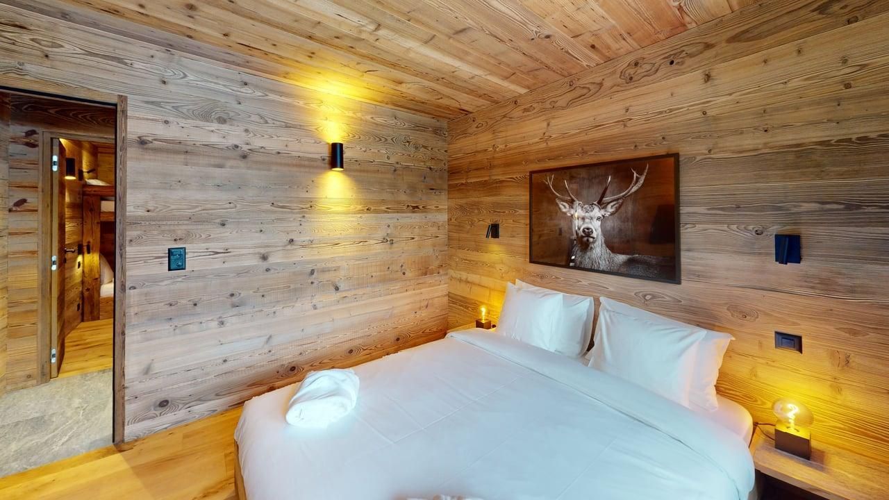 A cozy bedroom with wooden walls, a white bed, and a deer portrait hanging above the headboard.