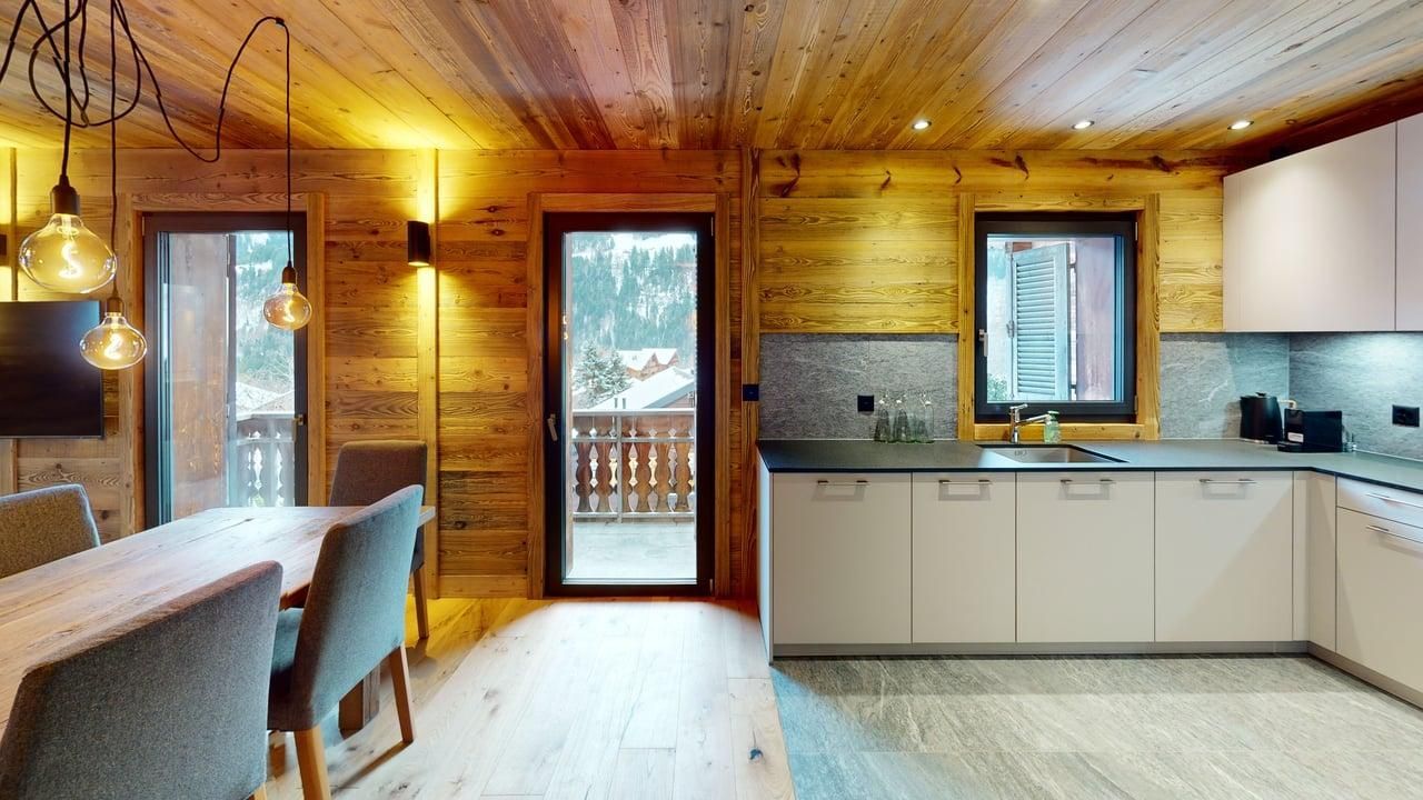 A modern kitchen and dining area in a rustic wooden cabin with light cabinets, a dining set, and views of the outdoors.