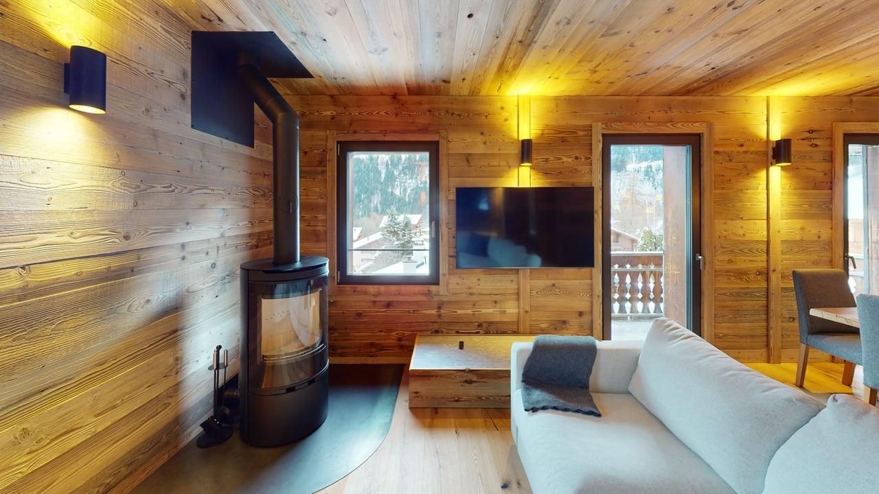 Modern rustic living room with wood paneled walls, a black fireplace, a light gray sofa, and a wall-mounted TV.