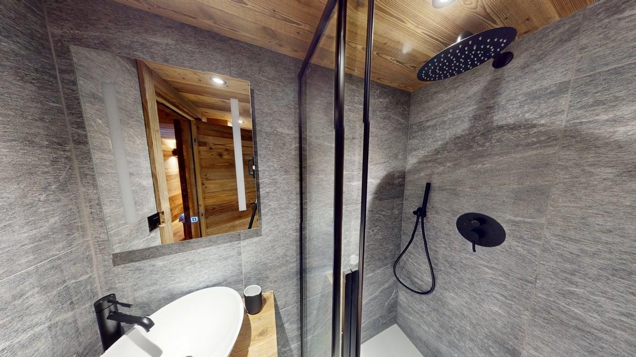 Une salle de bains moderne avec des murs carrelés gris, un plafond en bois, un lavabo vasque blanc et une douche à effet pluie vitrée.