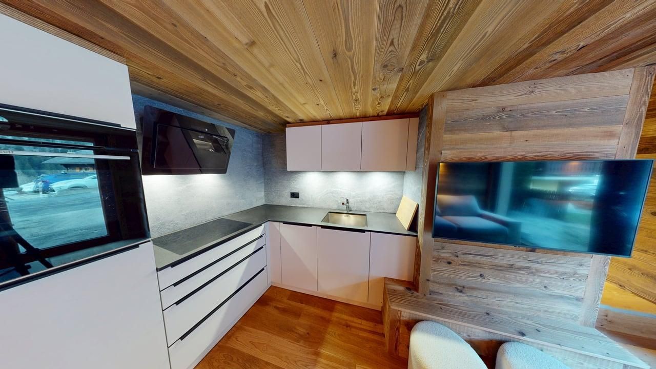 Une cuisine moderne avec des armoires blanches, des lambris aux murs et au plafond, et une télévision à écran plat fixée au mur.
