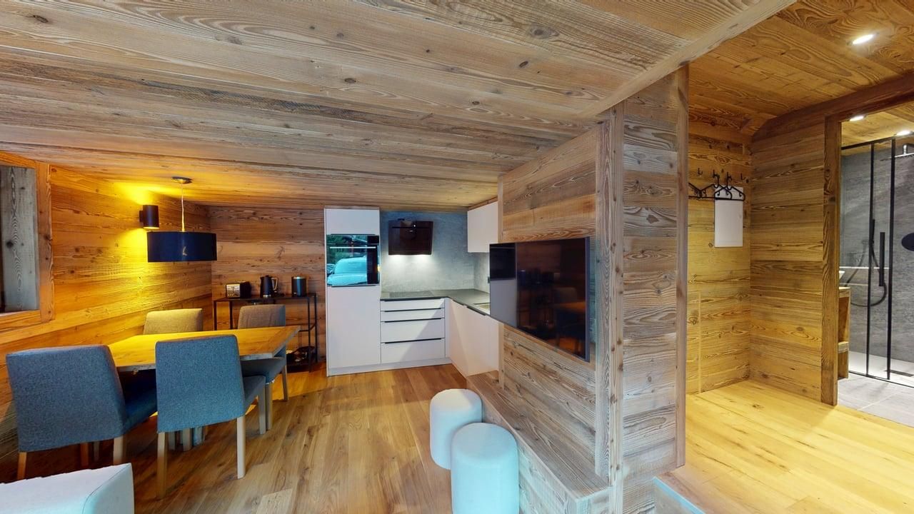 Intérieur d'appartement moderne de style rustique comprenant une petite cuisine, un coin repas et une vue sur une salle de bains carrelée.
