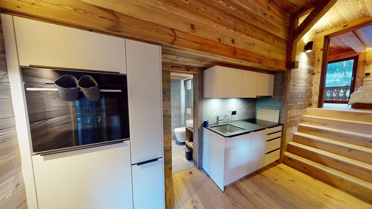 A modern kitchen with white cabinetry and appliances set against rustic wooden walls, featuring a doorway to a bathroom.