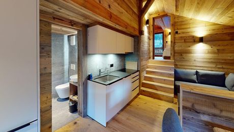 Une cuisine et un séjour dans une cabane rustique en bois, avec des placards blancs, un petit escalier et une porte de salle de bain.