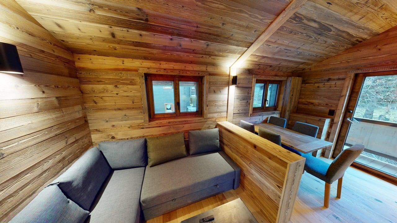 A rustic wooden room with a gray L-shaped sectional sofa and a small wooden dining set near a door.