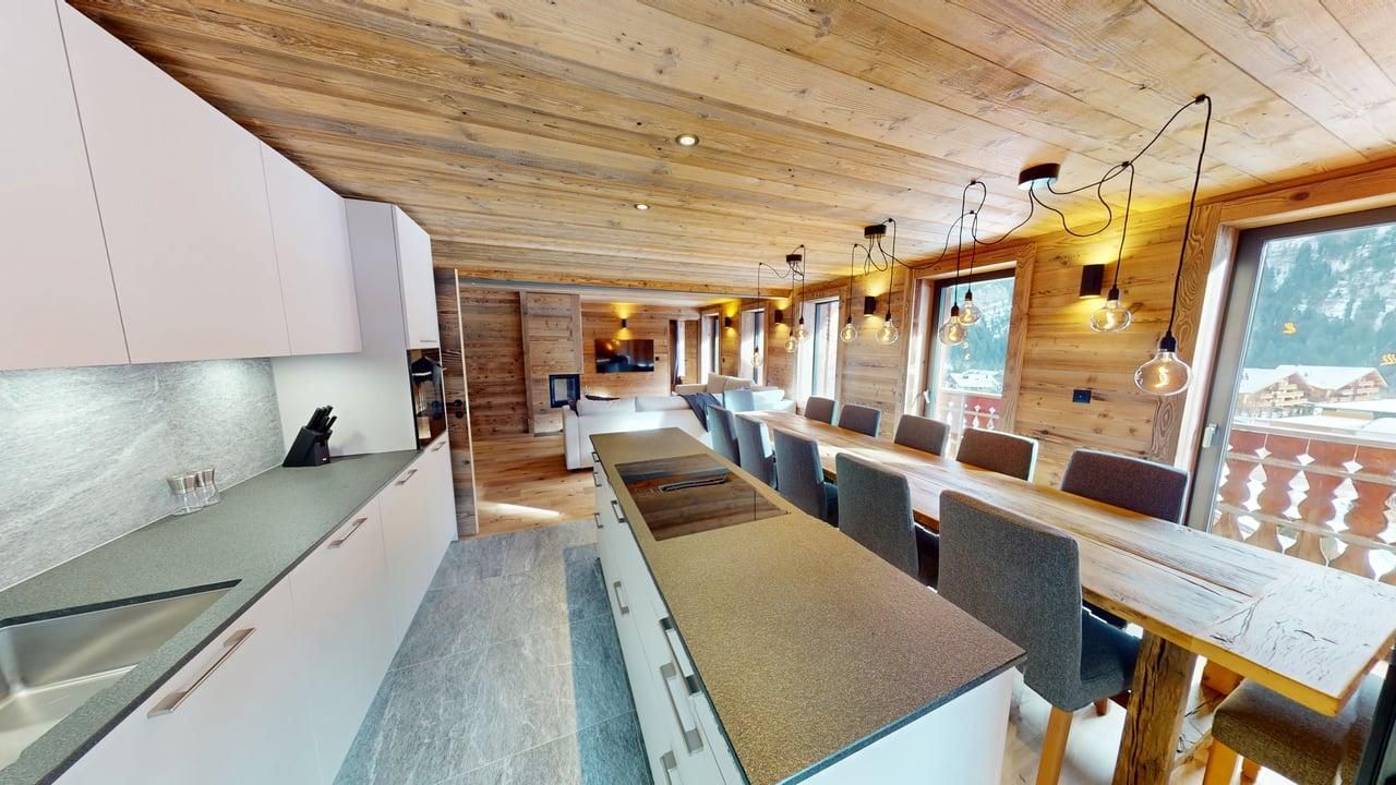 Une cuisine rustique et moderne avec des armoires blanches, un grand îlot et une longue table à manger en bois près d'une fenêtre lumineuse.
