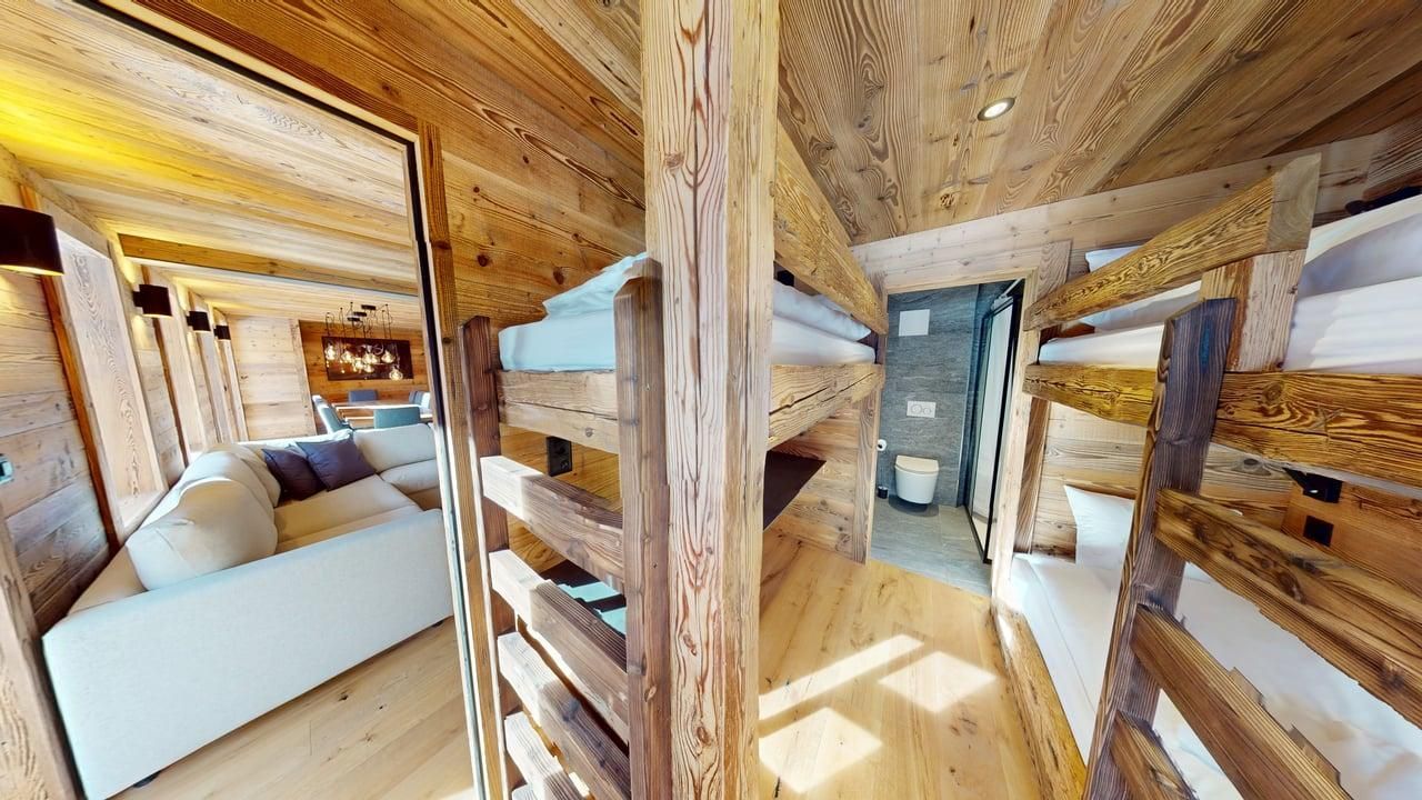 A rustic, wooden bedroom featuring a set of bunk beds, a view of a cozy couch in the next room, and a tiled bathroom.