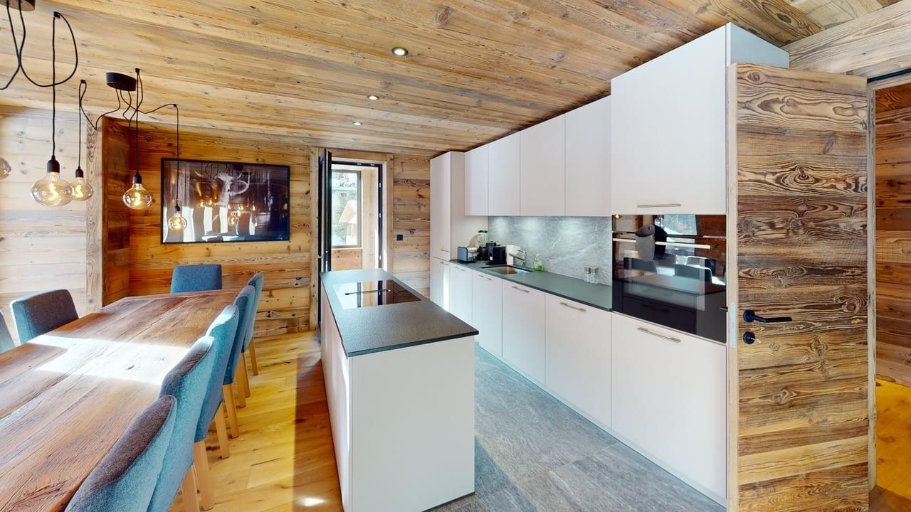 Modern rustic kitchen and dining room with wood-paneled walls, white cabinetry, a central island, and blue dining chairs.