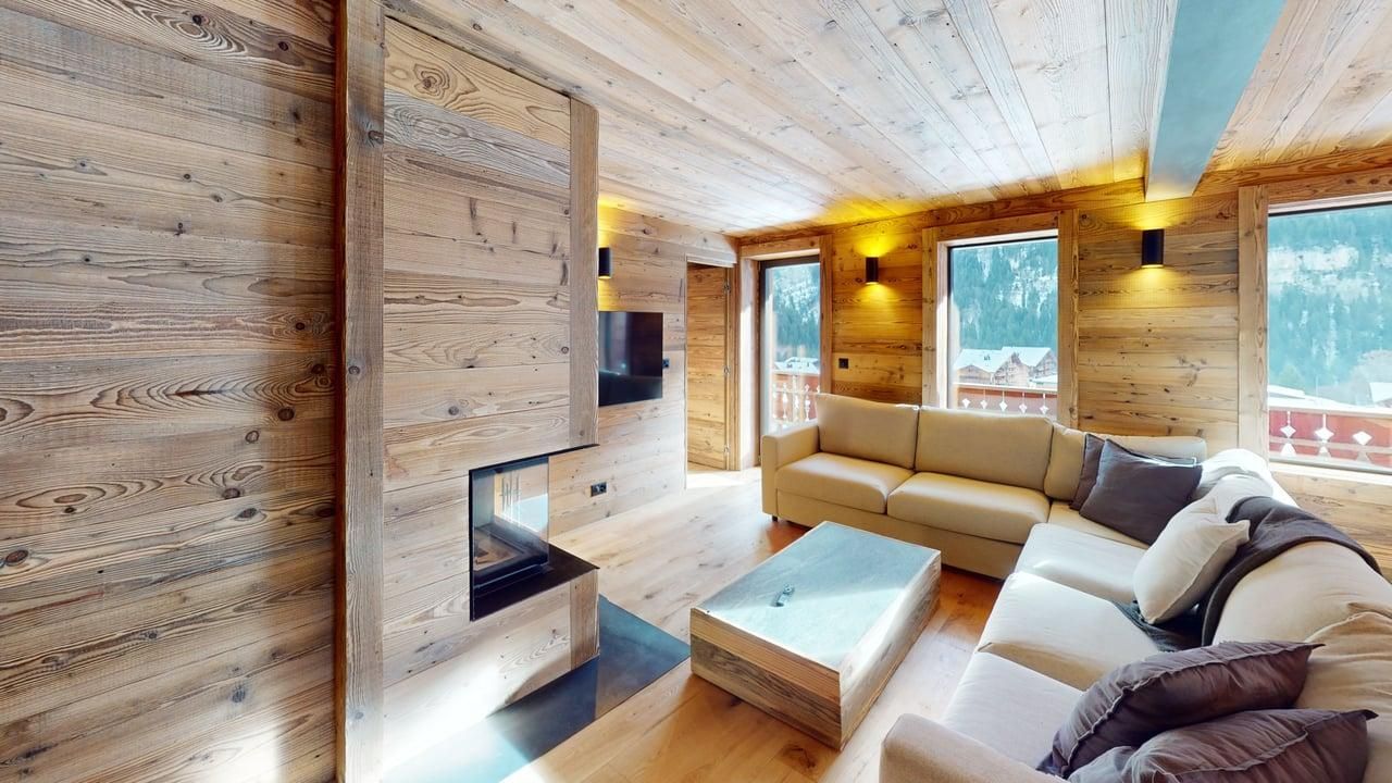 Un salon chaleureux avec des murs en bois clair, un canapé d'angle couleur crème, une table basse et une cheminée intégrée.