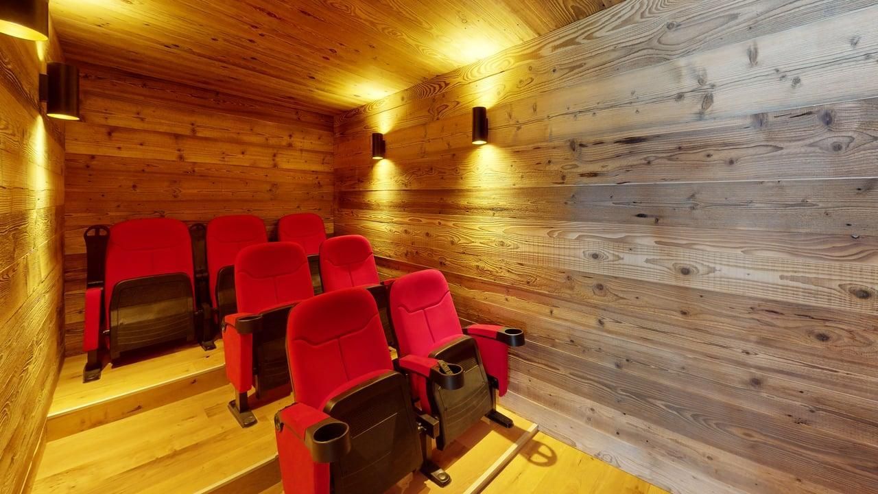 A small home theater with two rows of red velvet seats against rustic wood-paneled walls and warm, ambient lighting.