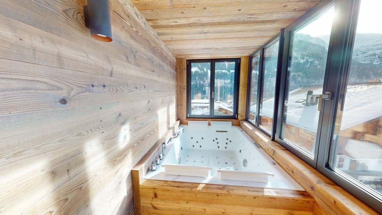 A wooden-paneled alcove featuring a built-in jetted tub next to a large window overlooking a snowy landscape.