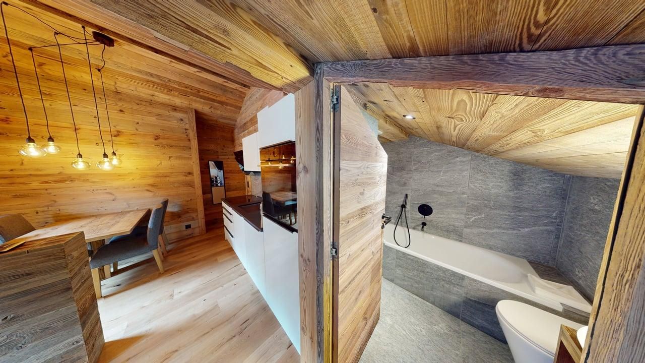 Vue à travers une porte donnant sur une salle de bains moderne avec baignoire, adjacente à une cuisine et un coin repas aux murs en bois.