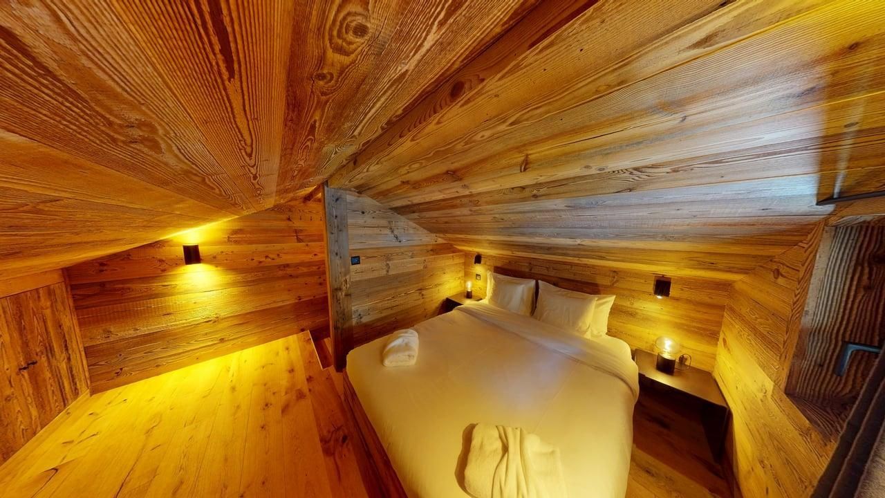 Une chambre confortable sous un plafond en bois incliné, avec un lit queen-size, un éclairage d'ambiance chaleureux et des lambris en pin clair.