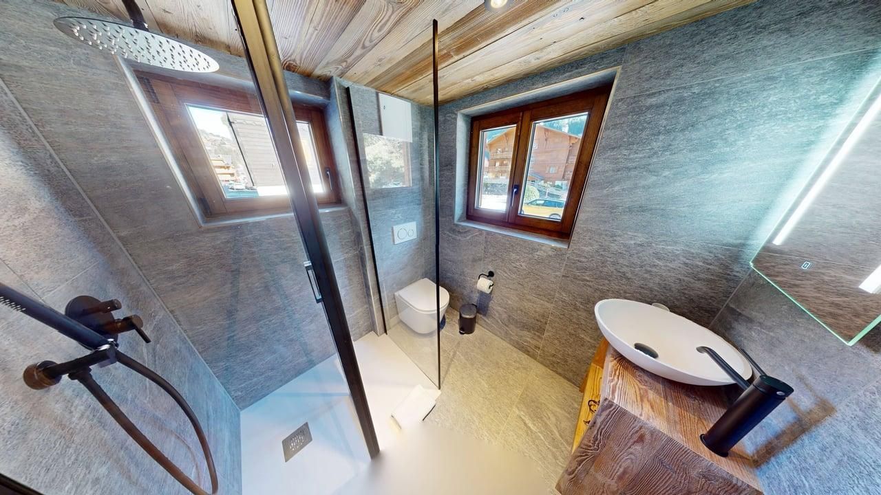 Une salle de bains moderne avec des murs gris effet pierre, une douche à l'italienne en verre, un lavabo vasque sur un meuble-lavabo en bois et des toilettes.
