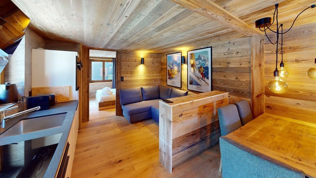 Intérieur rustique d'un chalet de ski en bois avec un canapé bleu, une table à manger, un comptoir de cuisine et une vue sur une chambre.