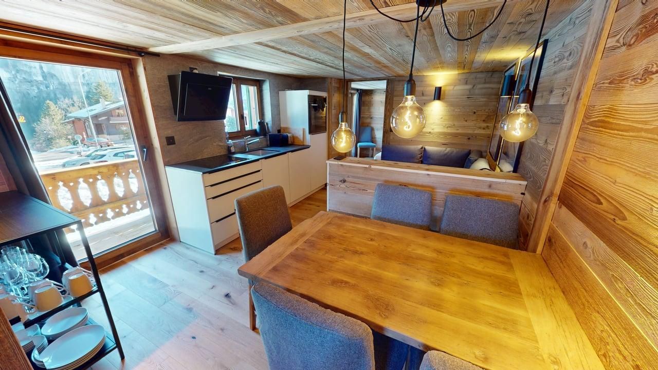 Intérieur chaleureux d'un chalet en bois avec table à manger, chaises, cuisine ouverte et balcon avec vue.