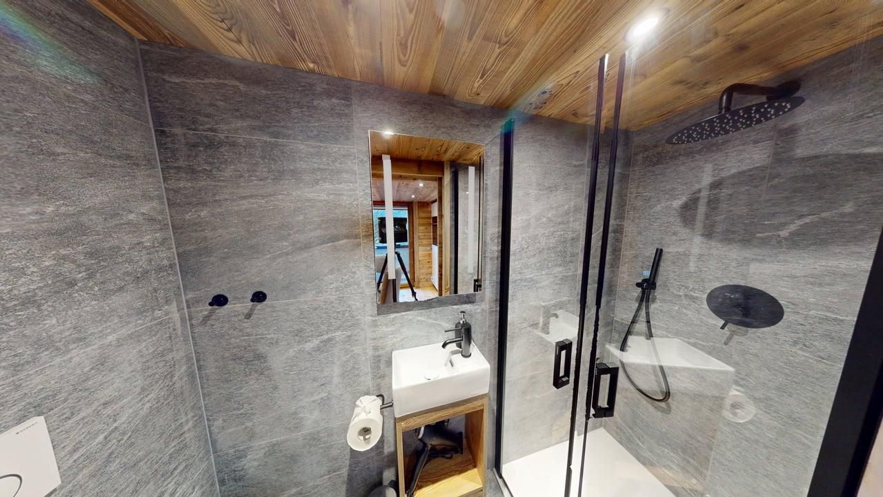 Une salle de bains moderne avec des murs en pierre grise, un plafond en bois, un lavabo carré blanc et une douche vitrée.