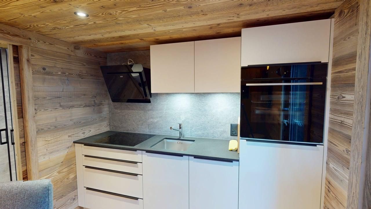 Une cuisine moderne avec des armoires blanches, des comptoirs foncés et un four mural, le tout sur fond de murs en bois clair rustique.