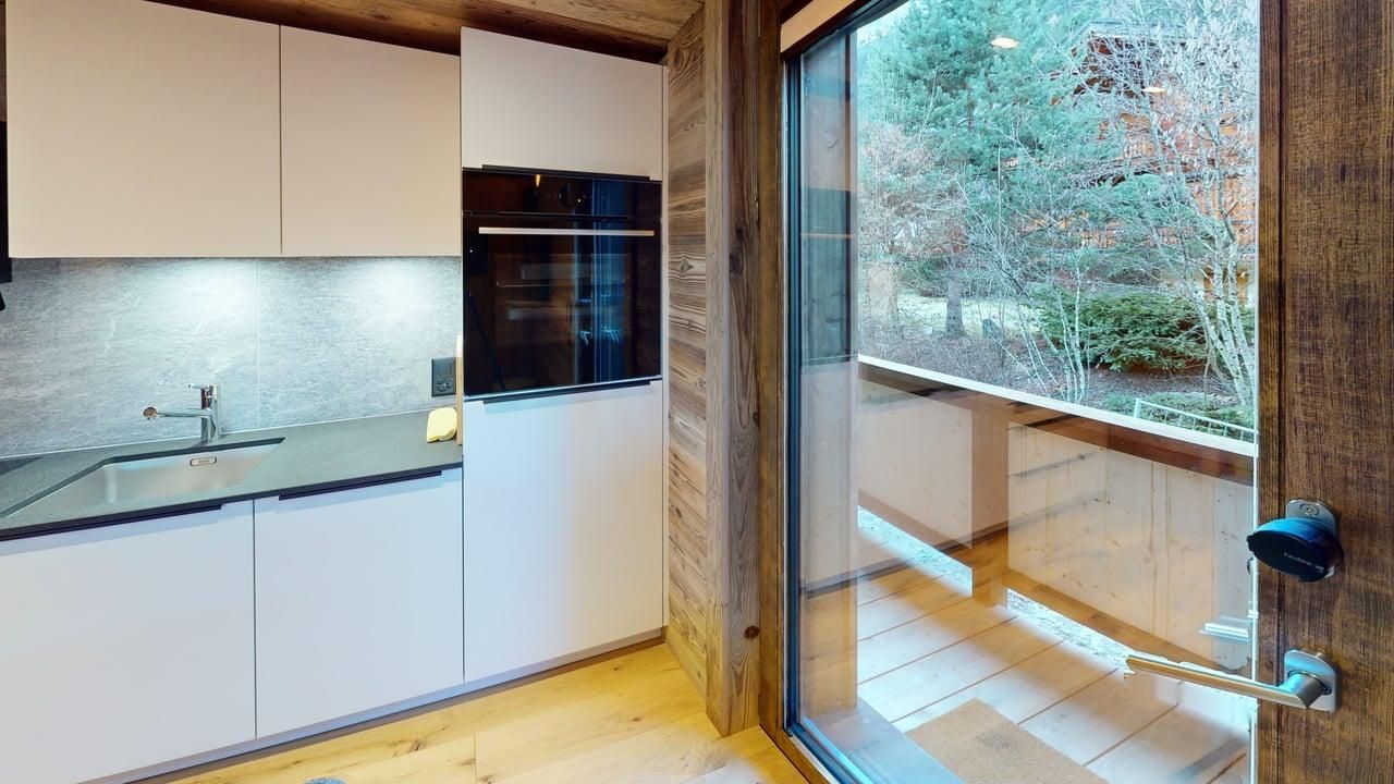Une cuisine moderne avec des placards blancs et un four encastré foncé, jouxtant une grande fenêtre donnant sur les arbres.