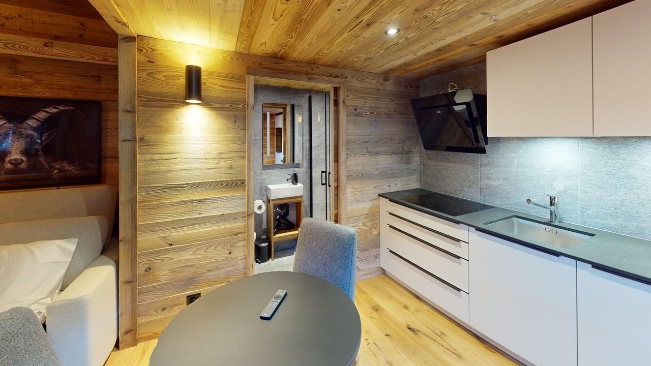 Une kitchenette moderne avec des placards blancs et un plan de travail foncé jouxte un coin repas avec une table ronde dans un chalet en bois.