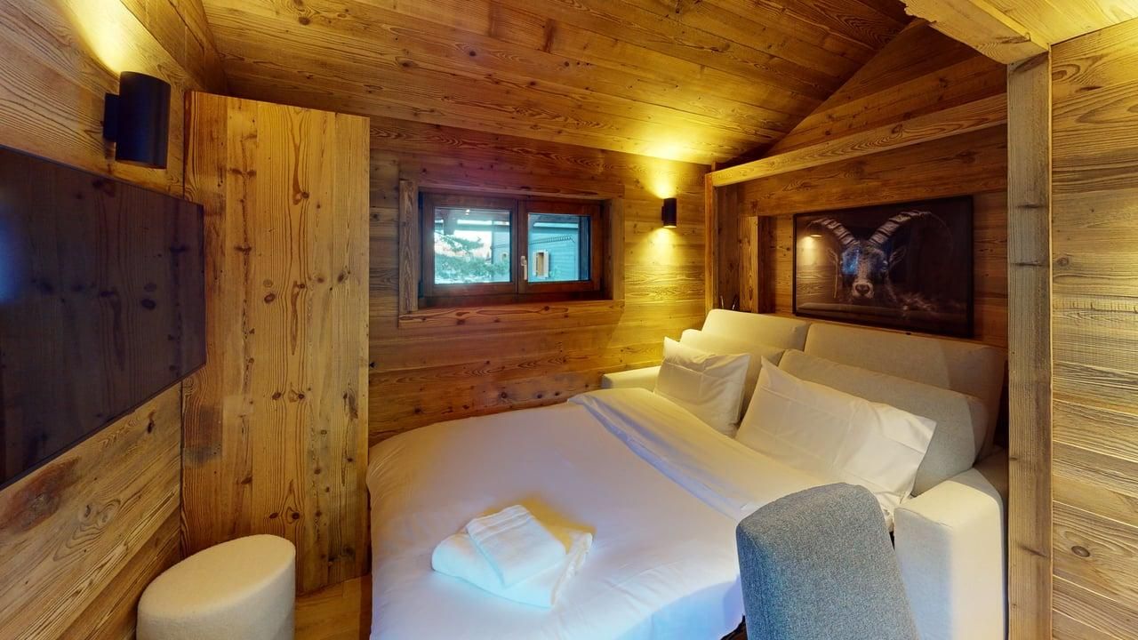 Une chambre confortable aux murs lambrissés, avec un lit soigneusement fait et des draps blancs, une petite fenêtre et des œuvres d'art accrochées au mur.
