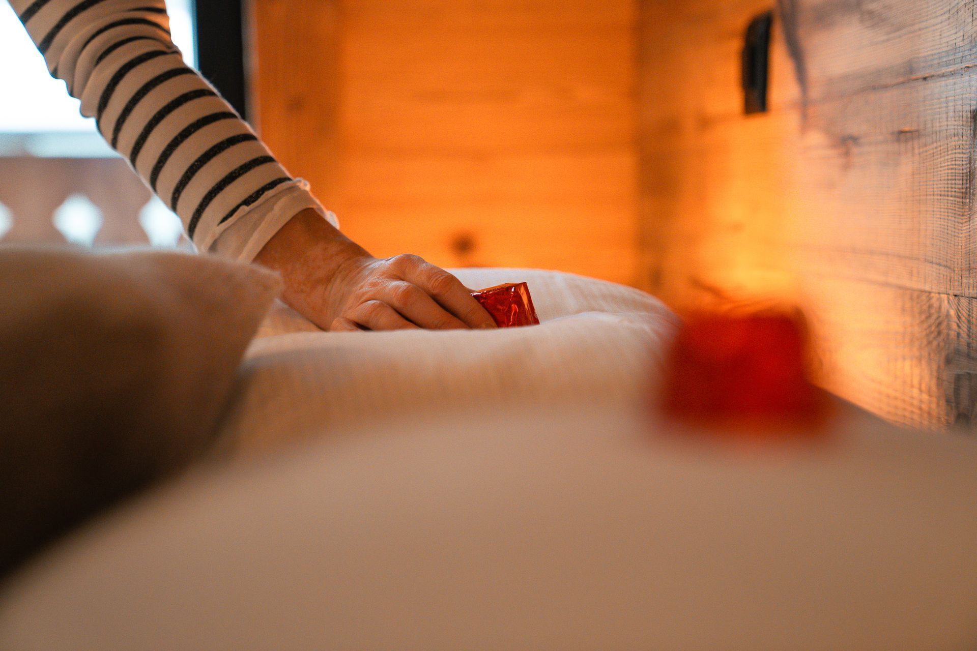 A person in a striped sleeve reaches toward a red object on a white surface inside a warm, wood-paneled room.