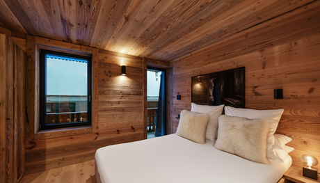 Chambre confortable avec murs et plafond en bois, un lit blanc avec des oreillers moelleux, une fenêtre et un éclairage d'ambiance doux.