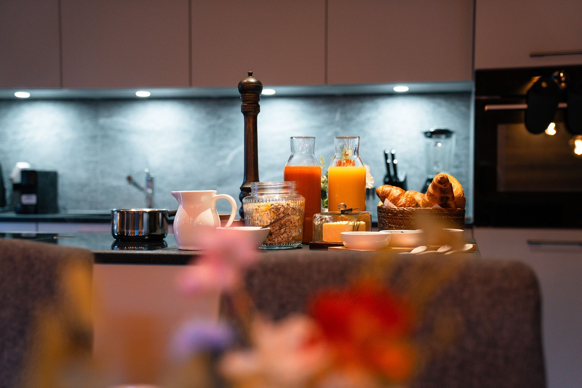 A kitchen counter topped with breakfast items, including juice, cereals, and pastries, with blurred flowers in the front.
