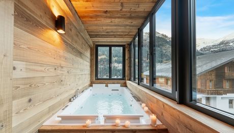 Un bain à remous rectangulaire se trouve dans une pièce lambrissée avec de grandes fenêtres donnant sur un paysage de montagnes enneigées.
