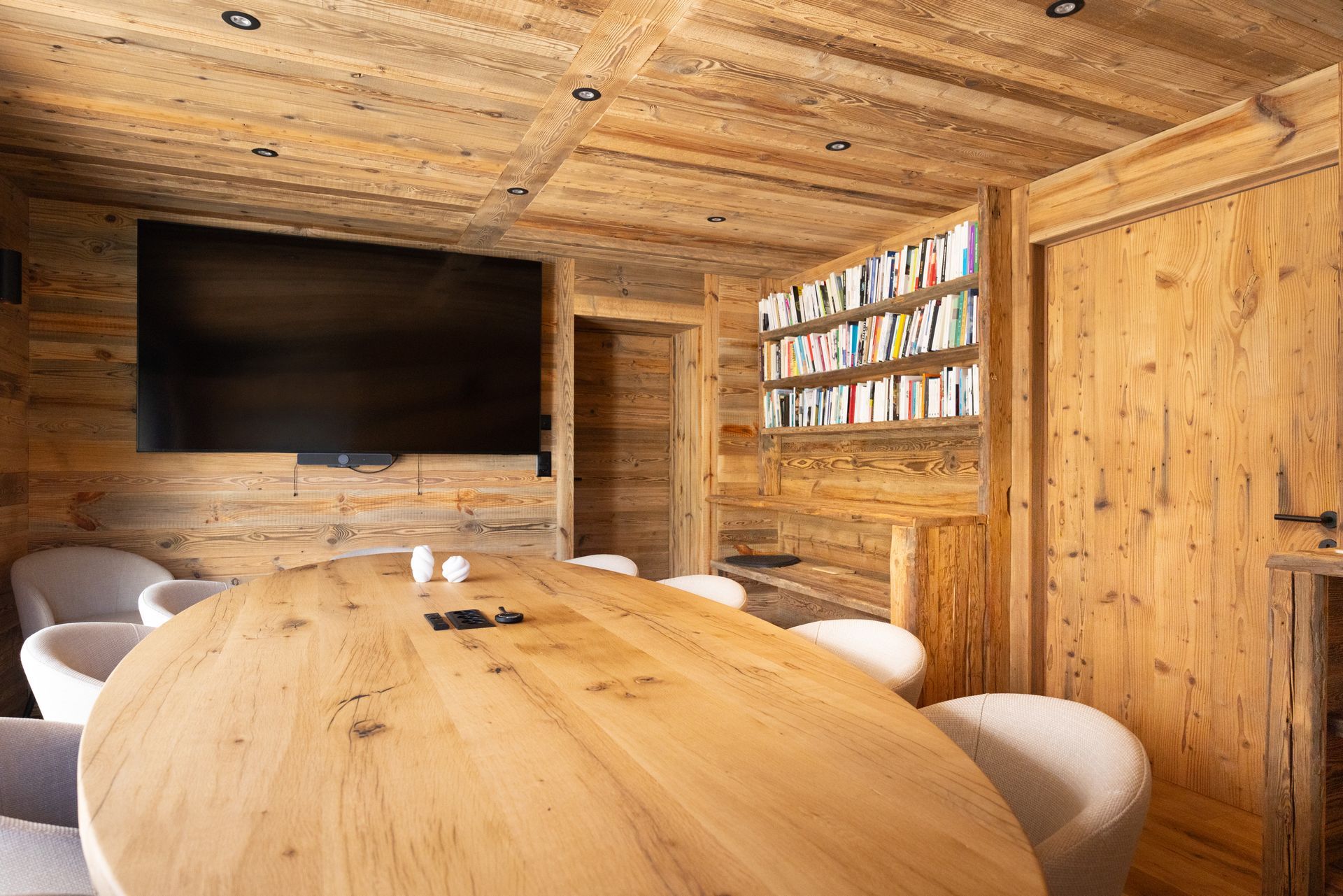 Wood-paneled meeting room with large oval table, wall-mounted TV, and bookshelves