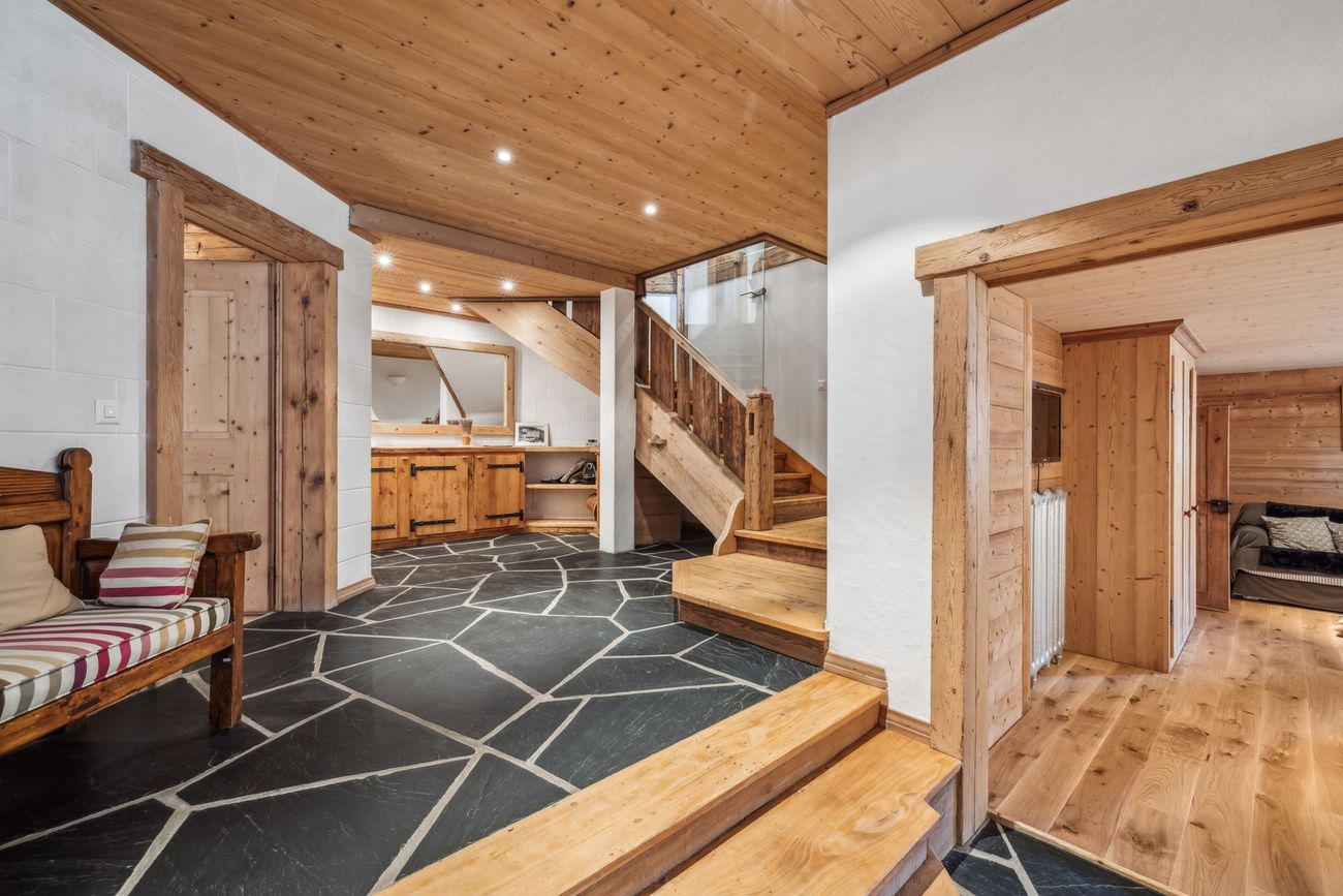Un couloir intérieur rustique avec un sol en ardoise, un plafond lambrissé et un escalier en bois menant à l'étage.