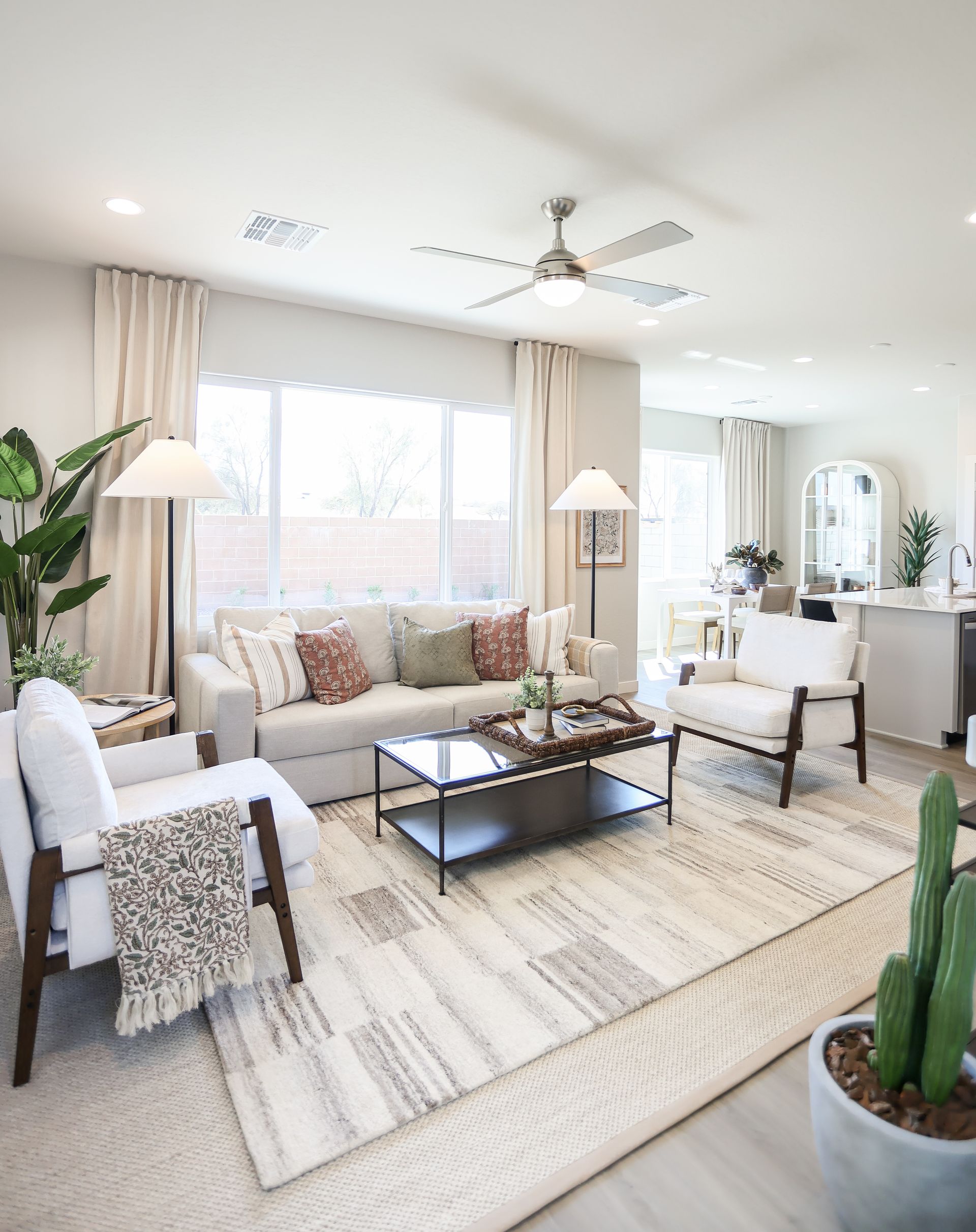 Bright living room with white furniture, large window, beige rug, and potted plants