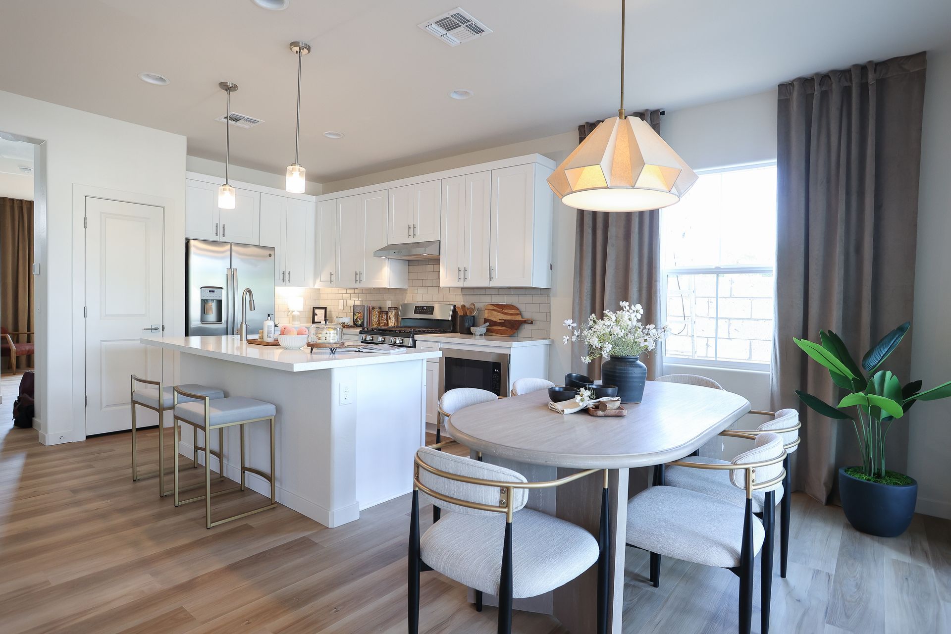 Bright open kitchen and dining area with white cabinets, island stools, round table, and large window.