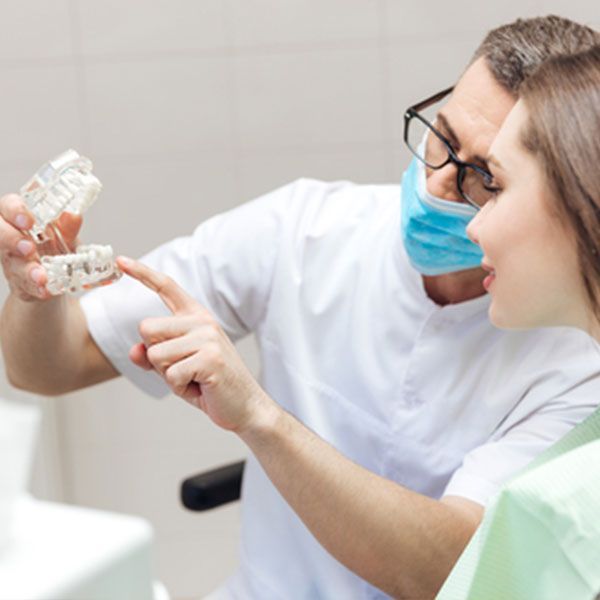 Dentist Wearing A Mask Is Showing A Patient A Model Of Their Teeth — Dentist On Tweed in Tweed Heads, NSW