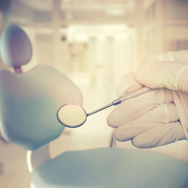 Dentist Is Holding A Dental Mirror In Front Of A Dental Chair — Dentist On Tweed in Tweed Heads, NSW