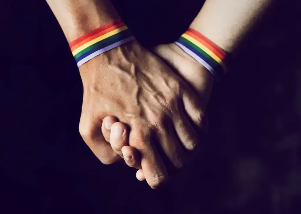 Hands with pride bands clasping, symbolizing the authentic connection and belonging needed for heali