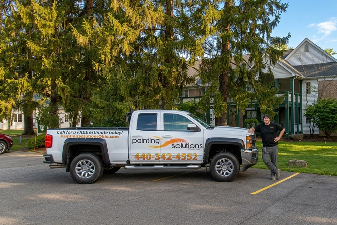 White pickup truck with company logo parked by a brick house; a man stands beside it in a driveway.
