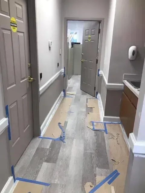Hallway under renovation with taped floor coverings, gray doors, and a doorway ahead.