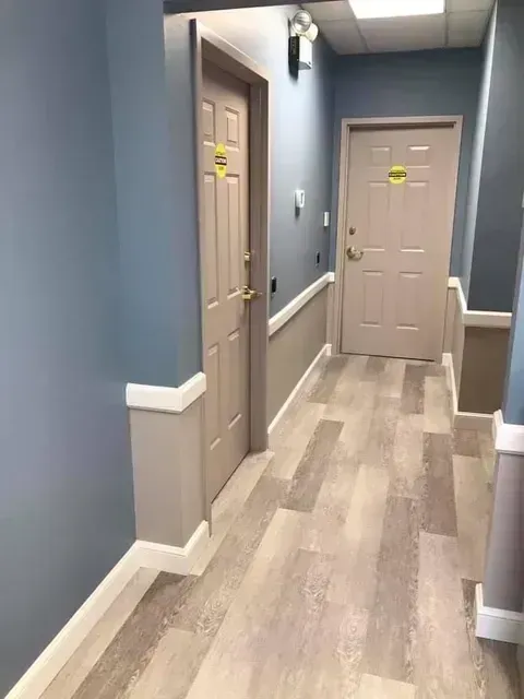 Narrow hallway with blue walls, beige doors, and wood-look flooring in an indoor building corridor